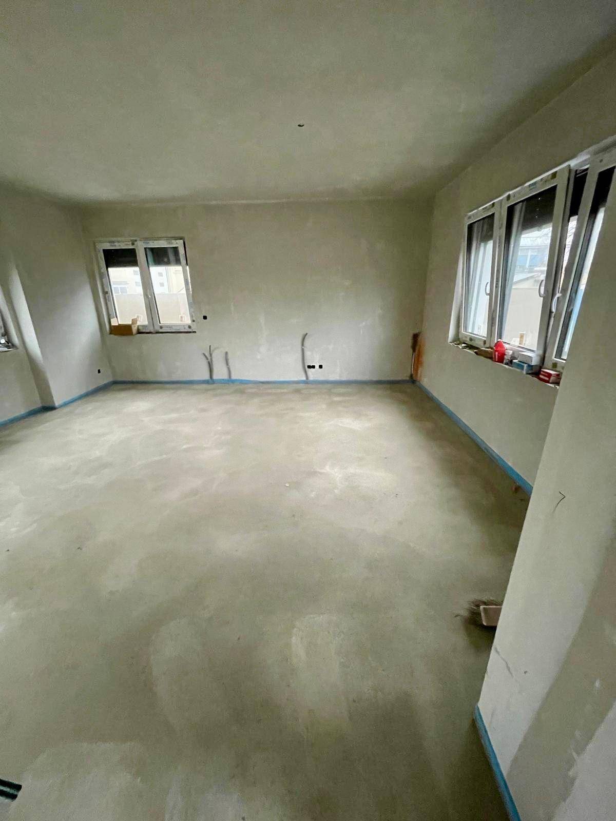 Geräumiger Rohbau-Raum mit Estrichboden und mehreren Fenstern, bereit für den Innenausbau.