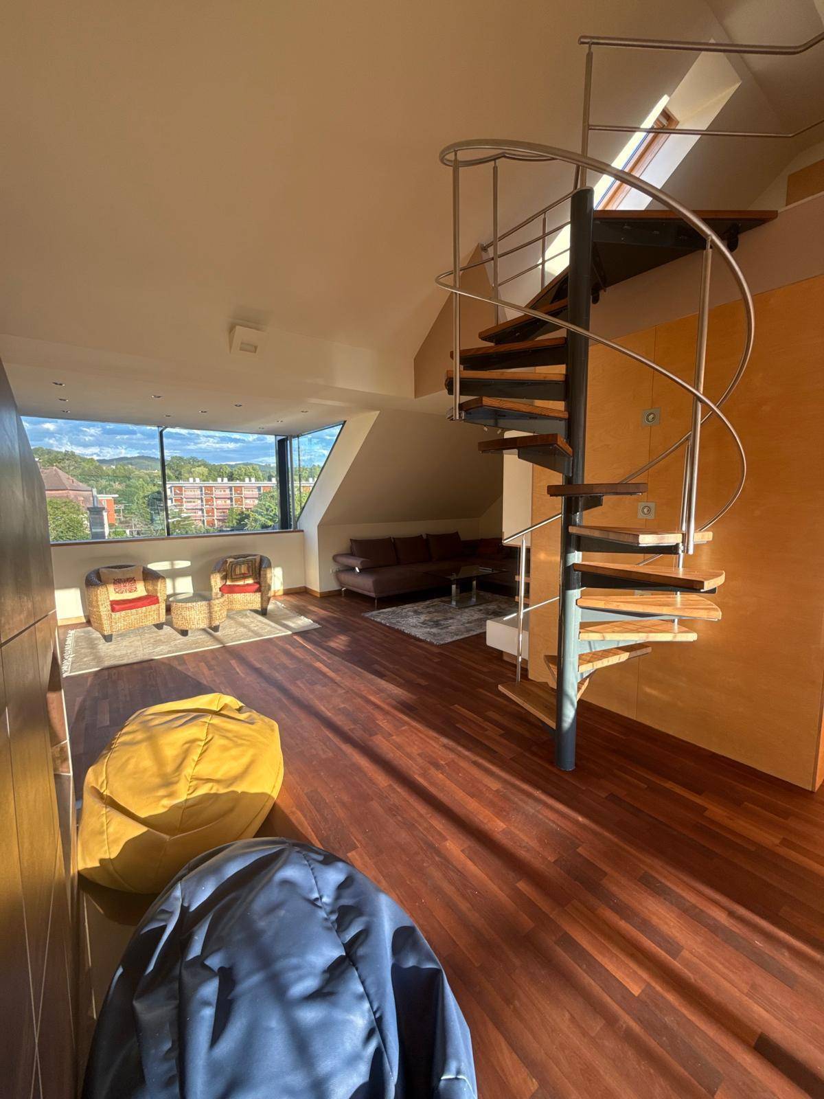 Geräumiges Wohnzimmer mit Holzboden, Wendeltreppe und großem Fenster mit Ausblick.