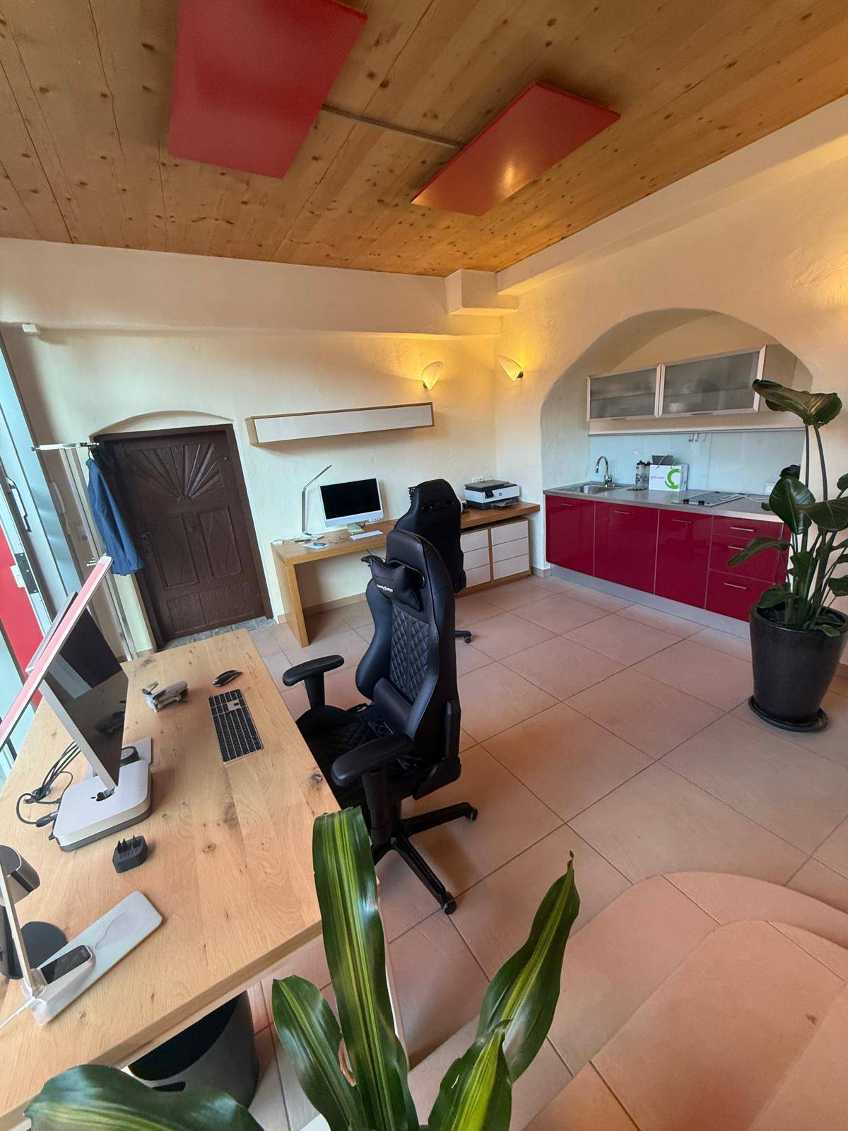 Geräumiges Büro mit Holzbalkendecke, integrierter Küchenzeile und mehreren Arbeitsplätzen.