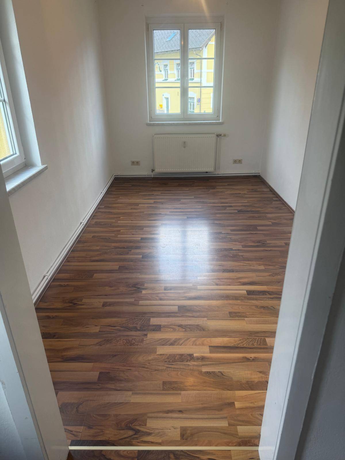 Unmöbliertes Schlafzimmer mit Holzboden und zwei Fenstern, bereit zur individuellen Gestaltung.
