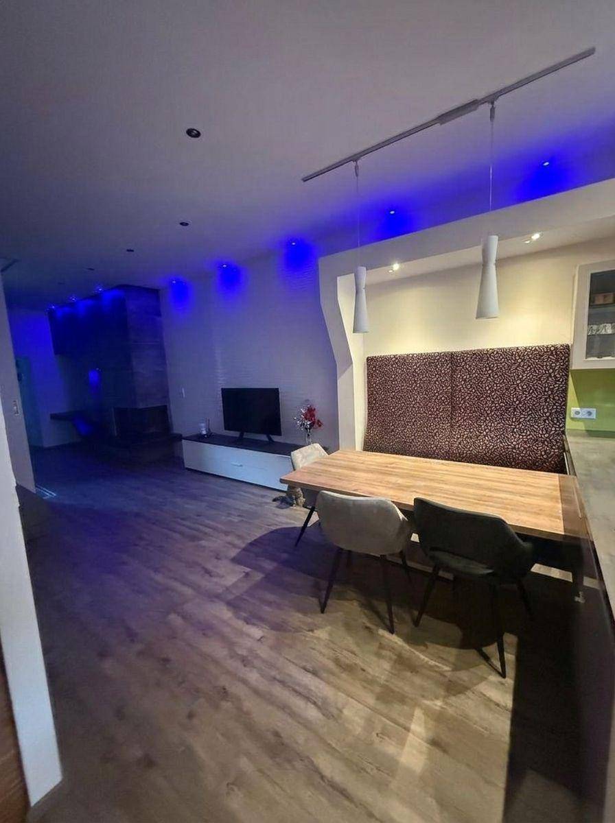 Geräumiger offener Wohn- und Essbereich mit Holzboden und moderner blauer Deckenbeleuchtung.
