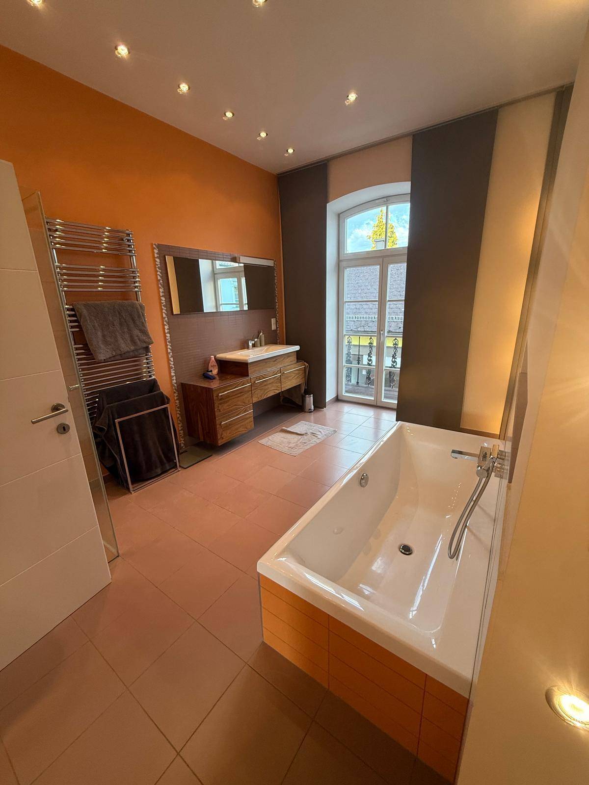 Modernes Badezimmer mit Badewanne, Waschtisch, beheiztem Handtuchhalter und Fenster.