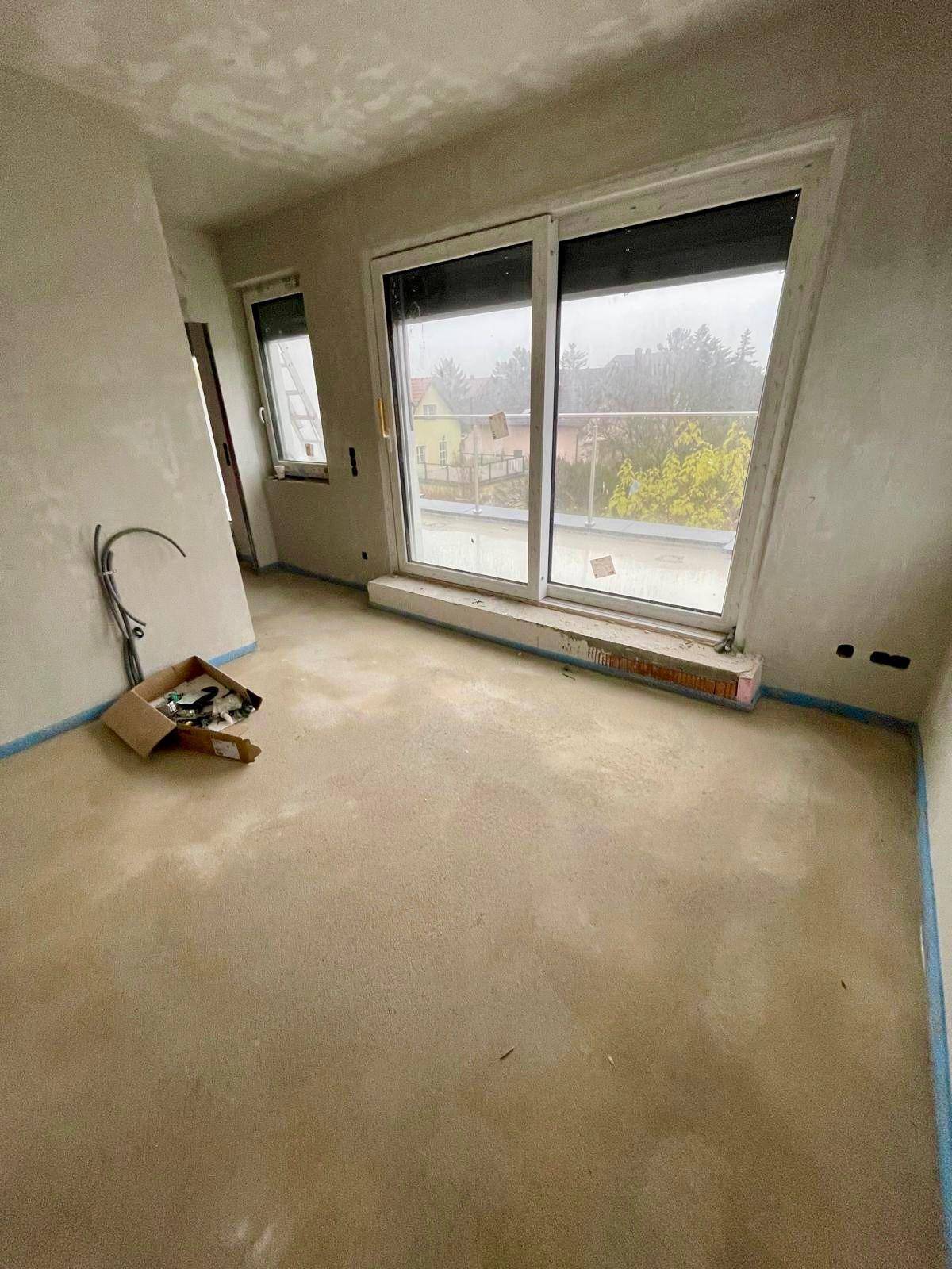 Rohbau-Zimmer mit großem Fenster und Zugang zu einem Außenbereich, mit Blick auf die Umgebung.