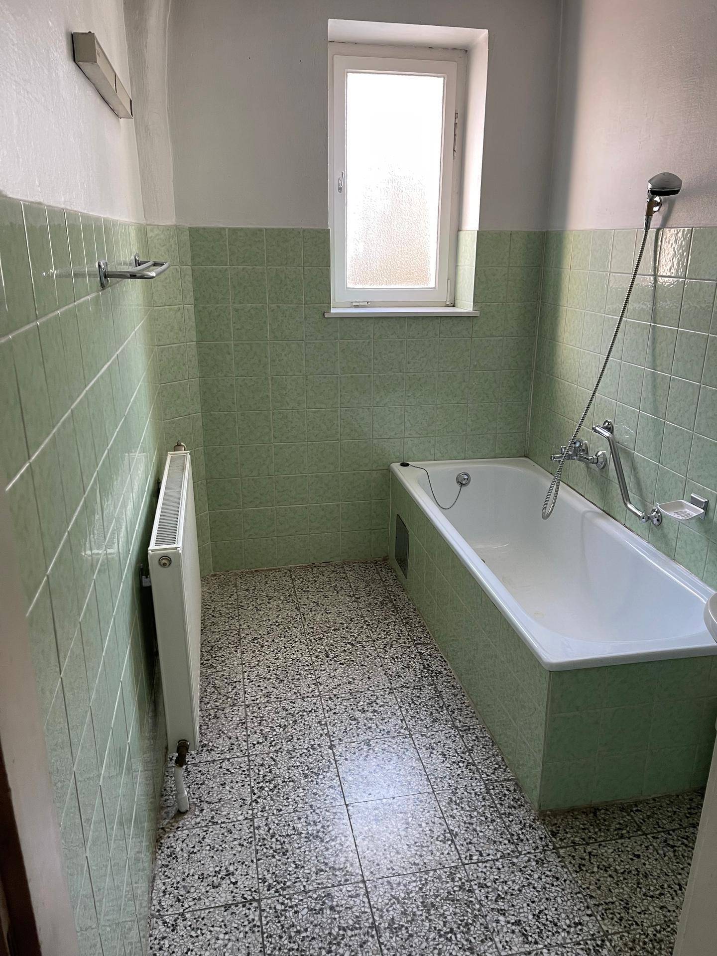 Badezimmer mit grünen Fliesen, Badewanne und Fenster.