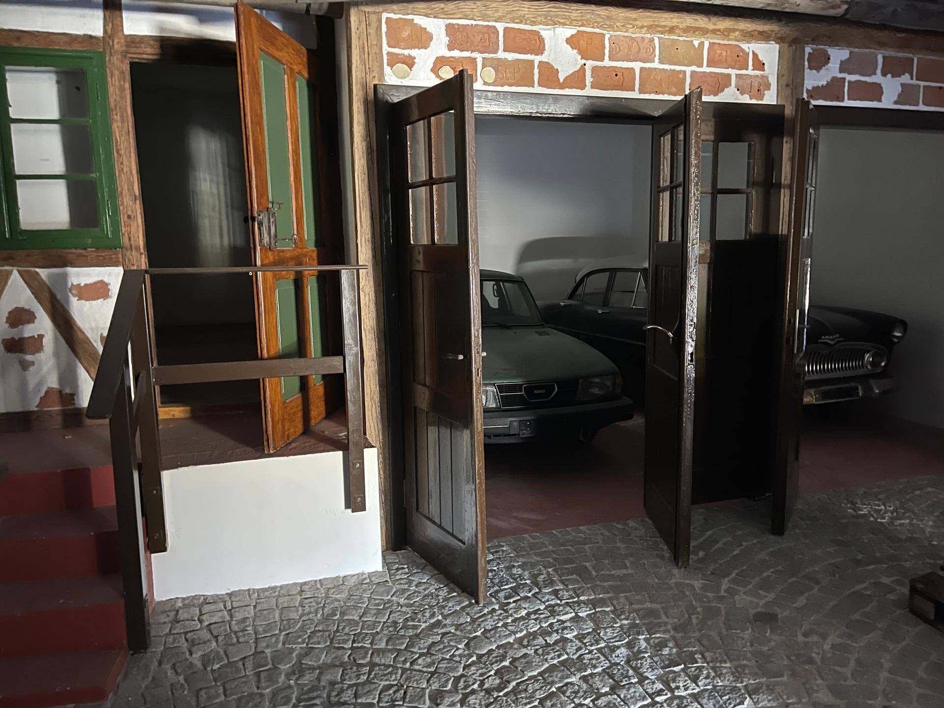 Thematischer Innenraum mit rustikalen Holztüren, einer kleinen Treppe und Oldtimern im Hintergrund.
