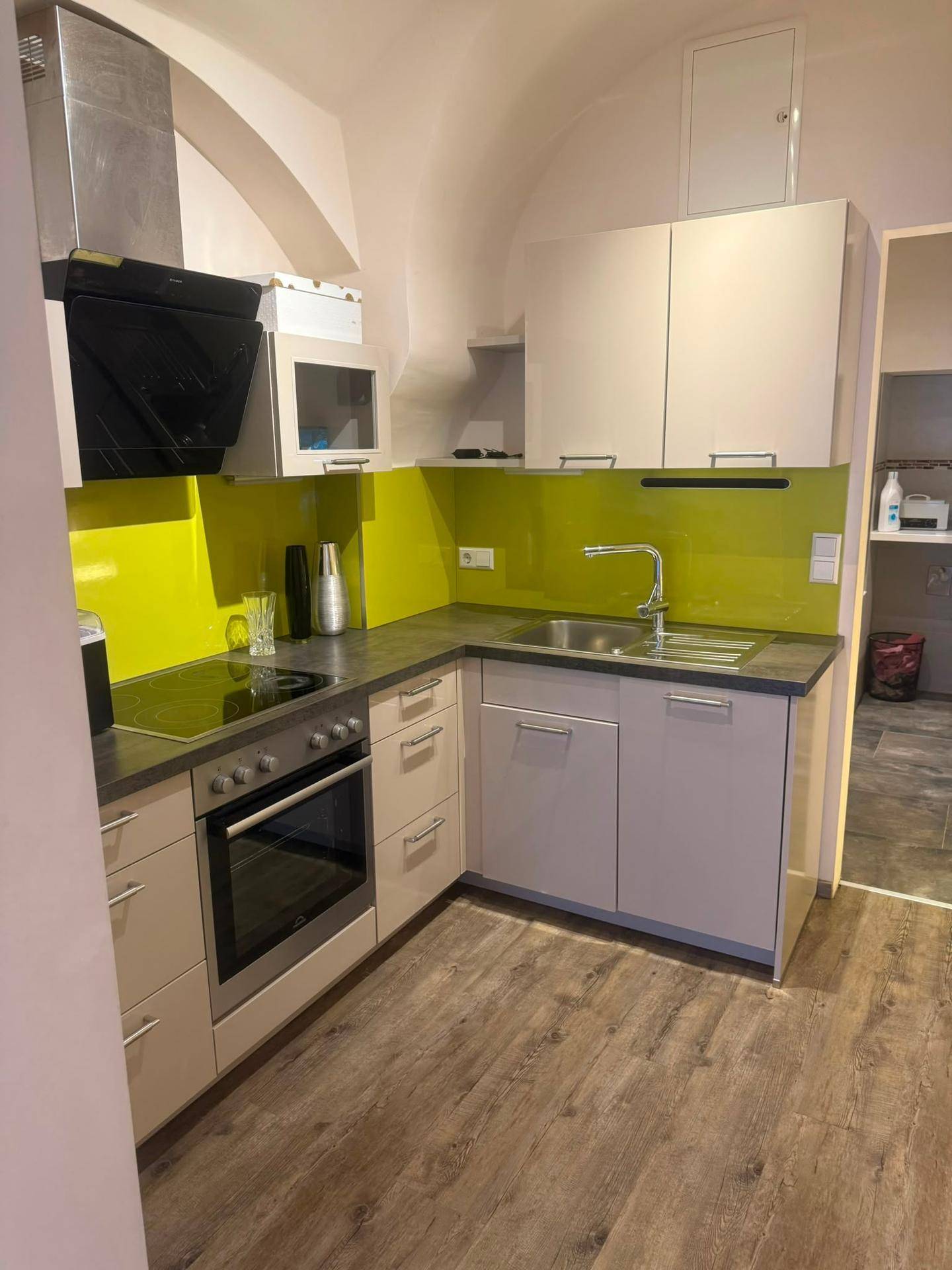 Funktionale Küche mit hellen Schränken, gelber Rückwand und Einbaugeräten unter gewölbter Decke.