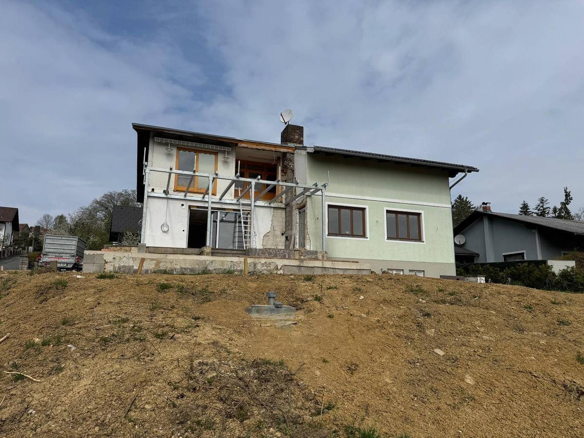 Hausfassade in Renovierung mit Gerüst und unfertigem Anbau auf einem unbebauten Grundstück.