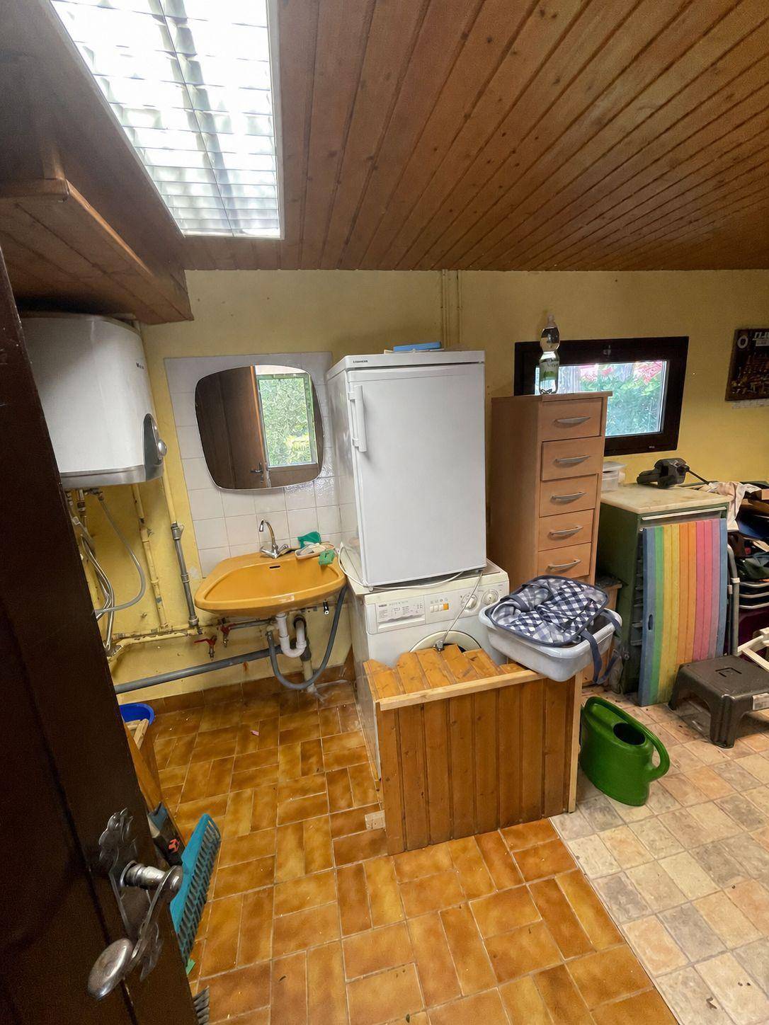 Rustikale Waschküche mit Waschmaschine, Trockner und Waschbecken unter einem Dachfenster.
