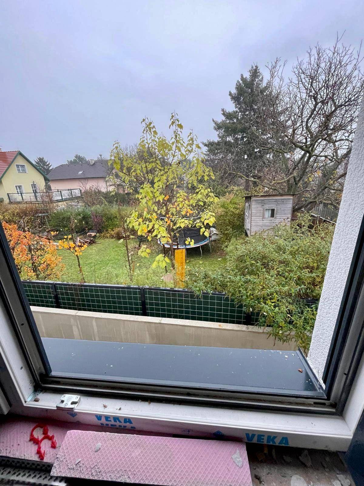 Blick aus einem Fenster auf einen grünen Garten mit Bäumen und einem Trampolin.