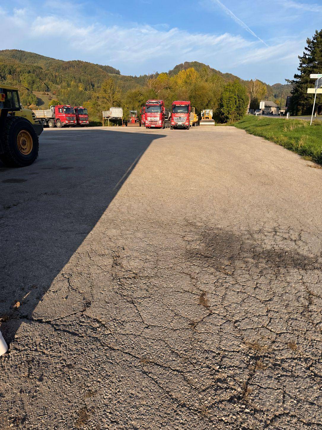 Ein großer asphaltierter Außenbereich mit mehreren Lastwagen und einer bergigen Landschaft im Hintergrund.