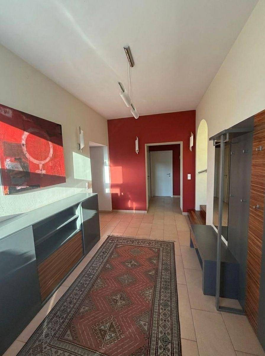 Heller Eingangsbereich mit Fliesenboden, moderner Garderobe und roter Akzentwand.