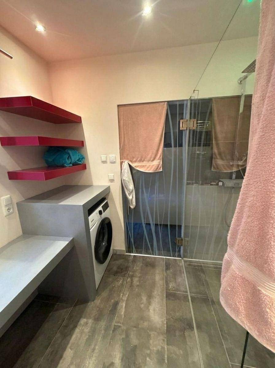 Funktionaler Hauswirtschaftsraum mit Waschmaschine, roten Regalen und Zugang zur Dusche.