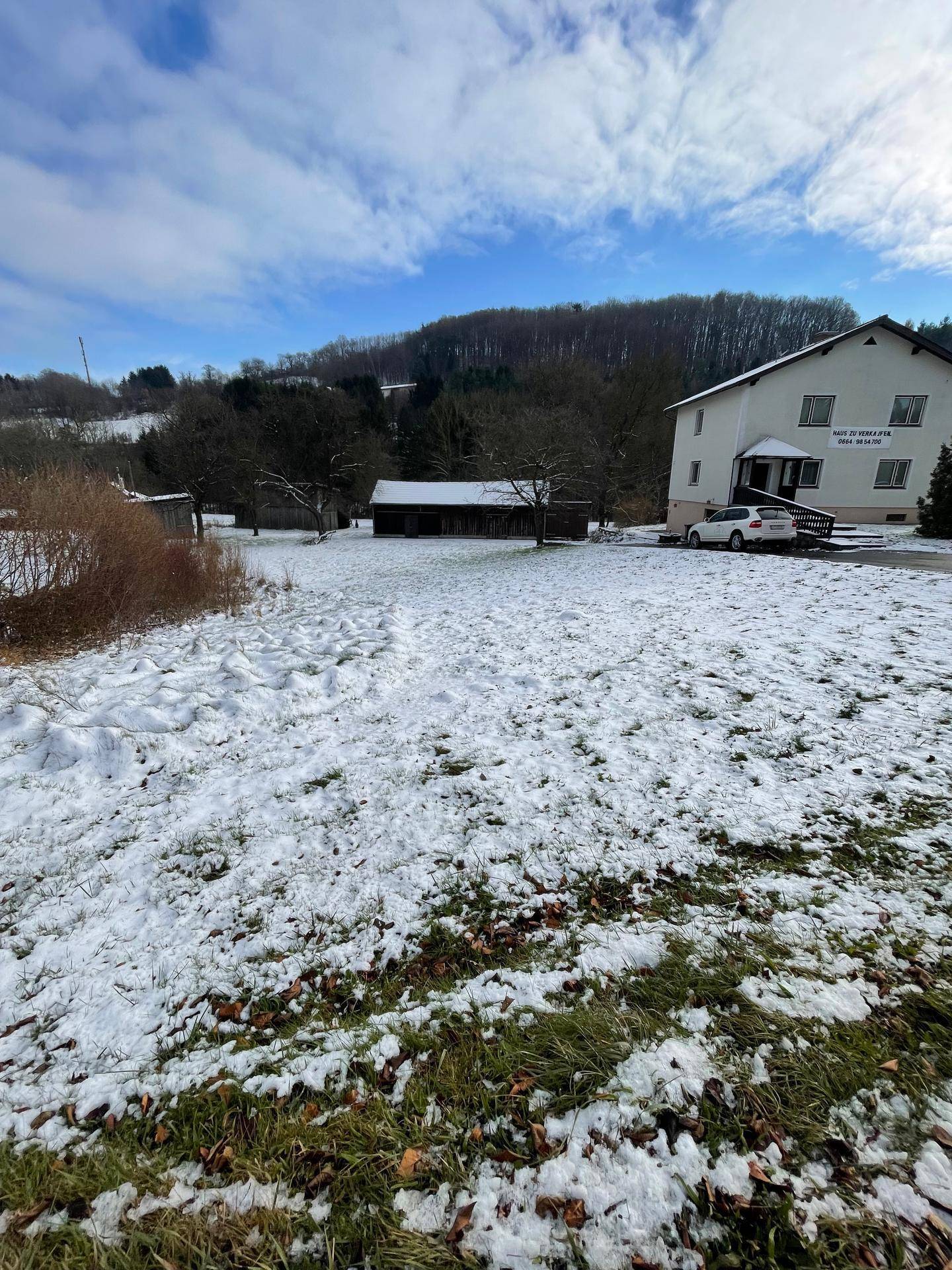 Wohnhaus mit schneebedecktem Grundstück und bewaldeten Hügeln unter einem klaren Winterhimmel.