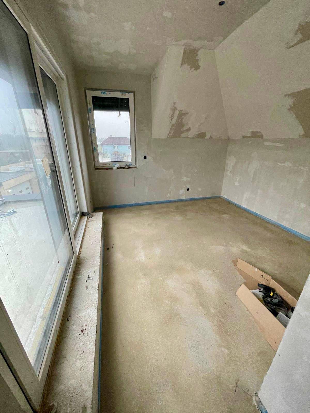 Rohbau-Zimmer mit Estrichboden, Zugang zu einem Außenbereich und Dachschräge.