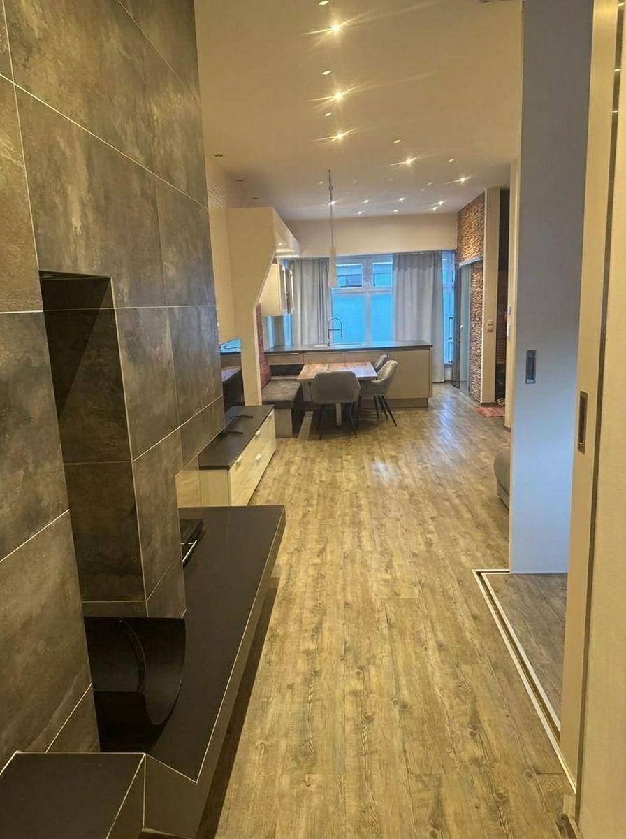 Heller offener Wohnbereich mit Holzboden, Kamin und Blick auf den Ess- und Küchenbereich.