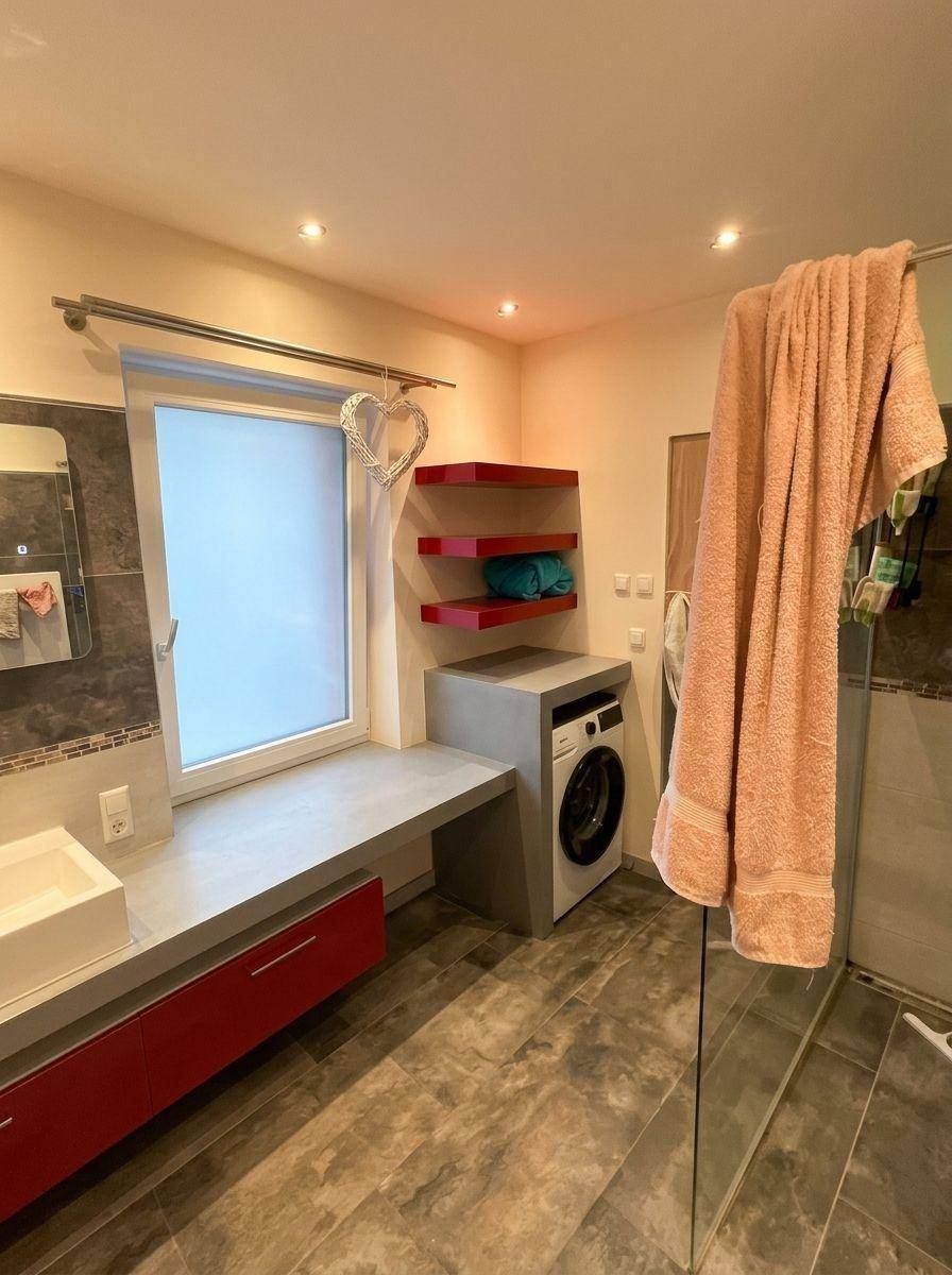Modernes Badezimmer mit Waschmaschine, Fenster, roten Regalen und großformatigen Fliesen.