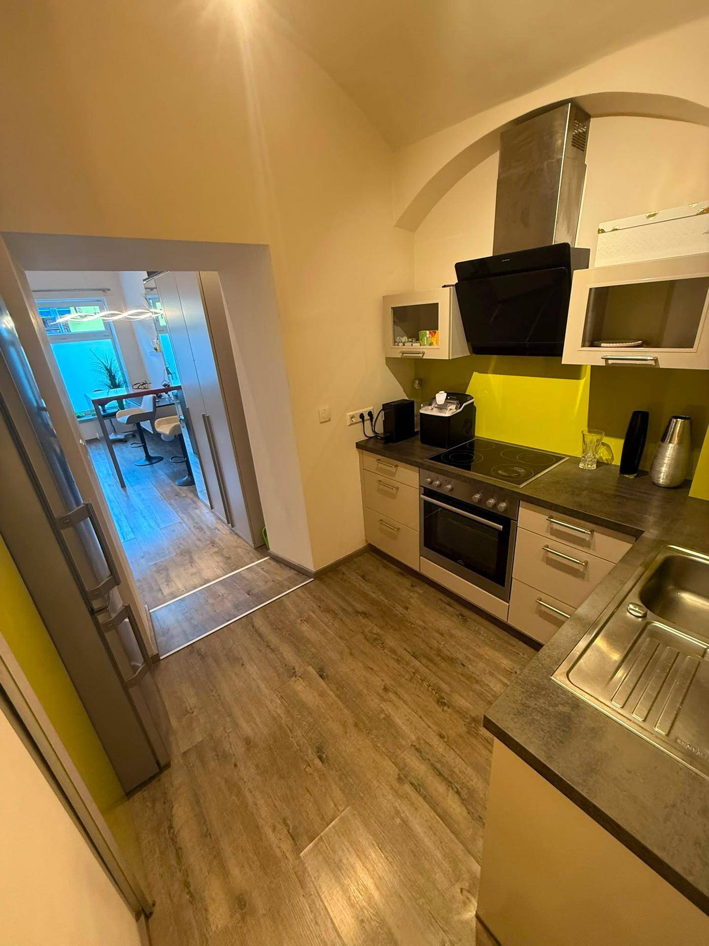 Küche mit Laminatboden, gelber Rückwand und Blick in einen angrenzenden Wohnbereich.