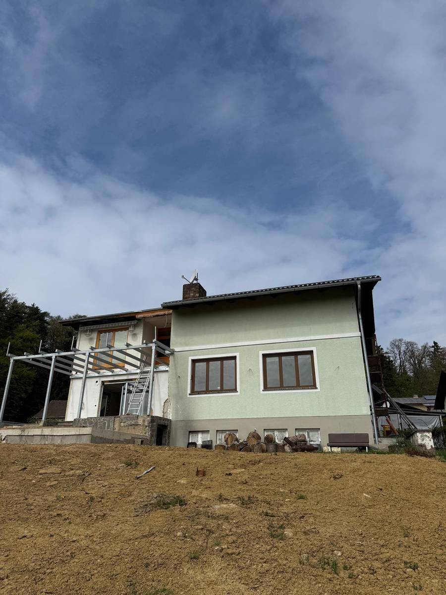 Rückansicht des Hauses in Bauphase mit unfertiger Terrasse und Blick auf die Umgebung.