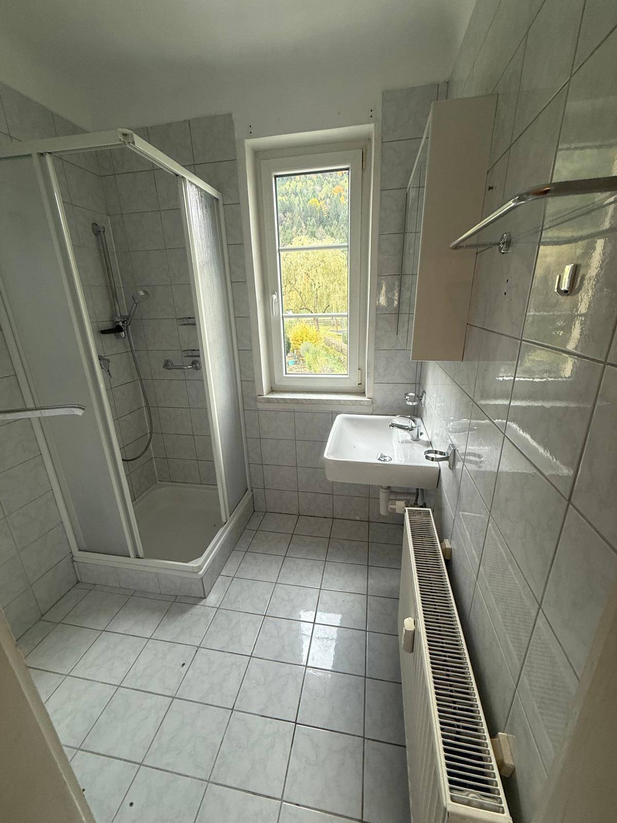 Älteres Badezimmer mit weißen Fliesen, Duschkabine und Waschbecken, bereit zur Modernisierung.