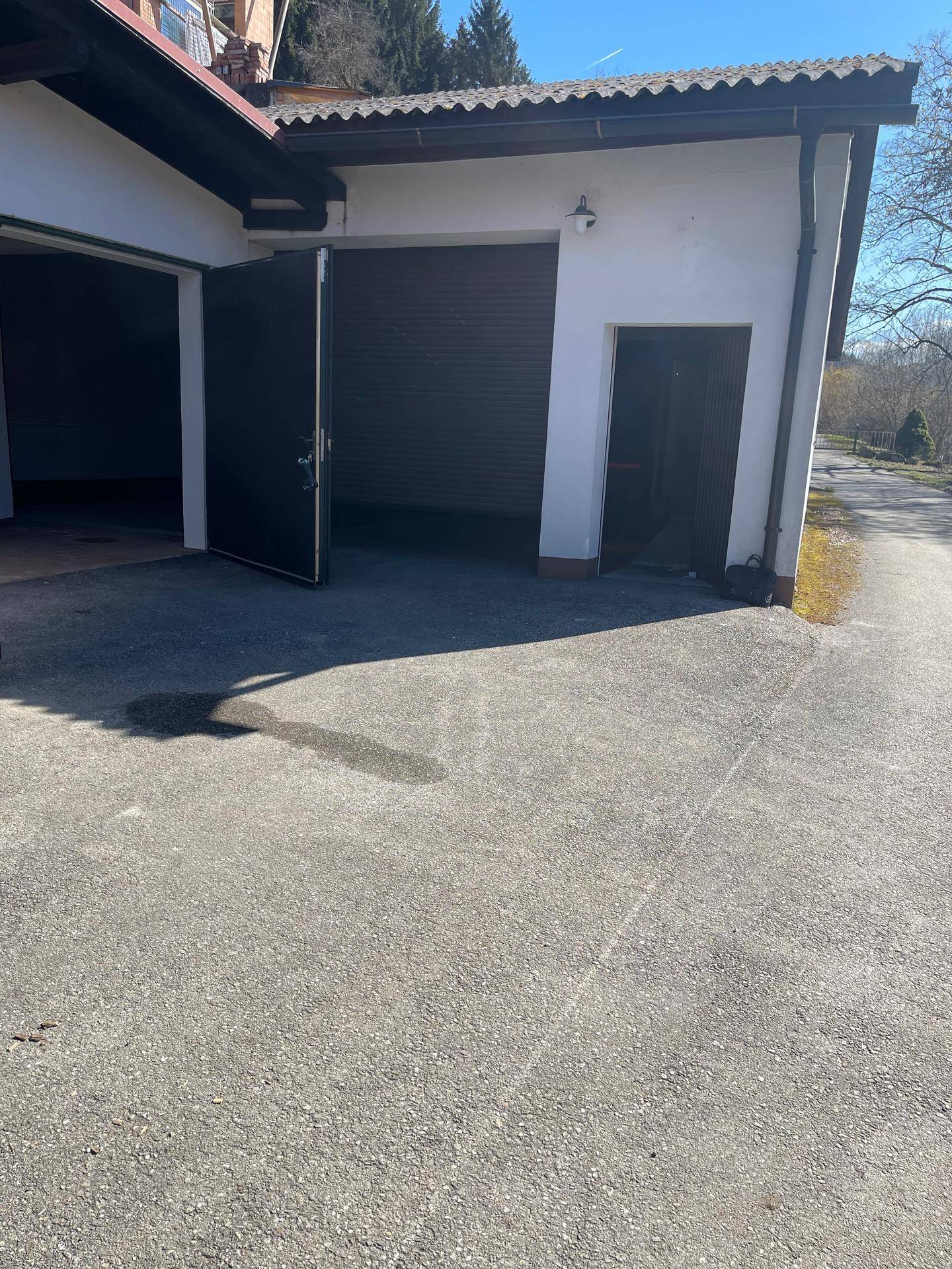 Außenansicht eines Gebäudes mit offener Garage und breiter Zufahrt an einem sonnigen Tag.