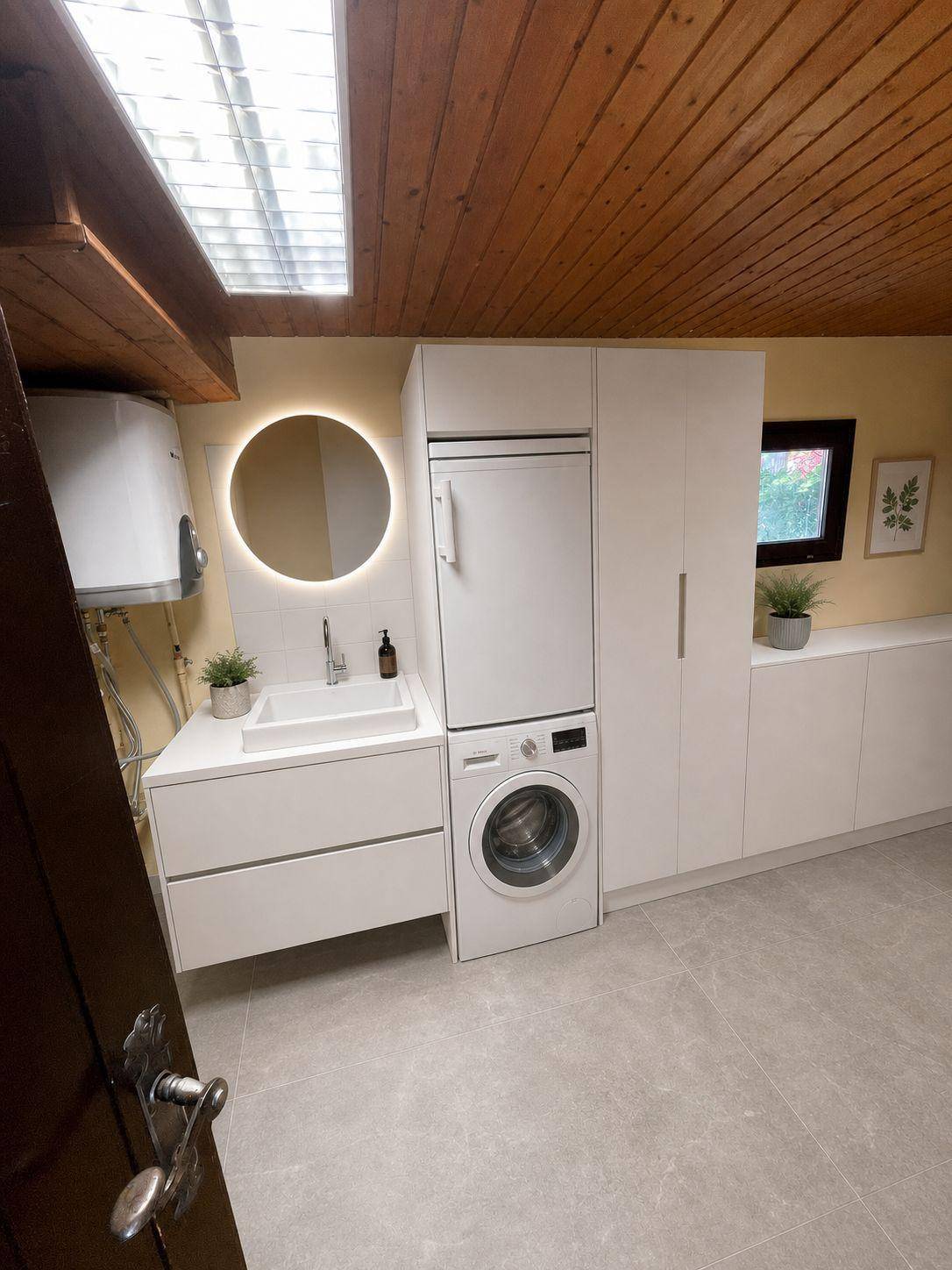 Moderne Waschküche mit Waschmaschine, Trockner und Waschbecken unter einem Dachfenster.