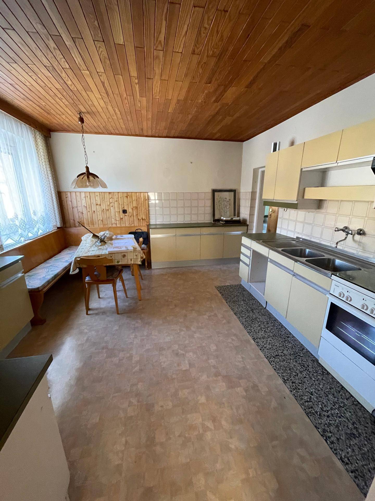 Küche mit Holzdecke, Essbereich und Einbauküche mit Spüle und Herd.