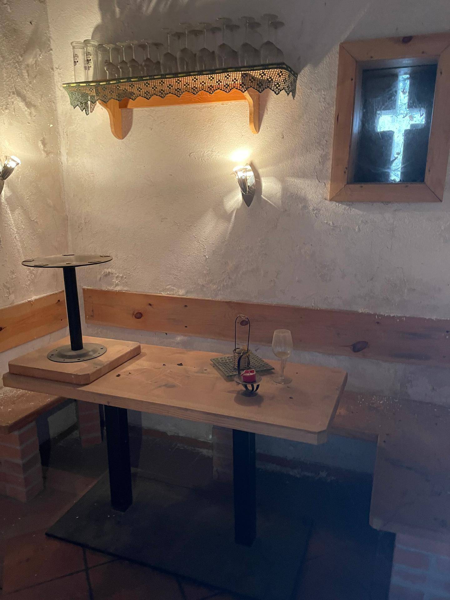 Rustikaler Sitzbereich mit Holztisch und Bänken, Wandleuchten und Gläserregal, ideal für gesellige Runden.