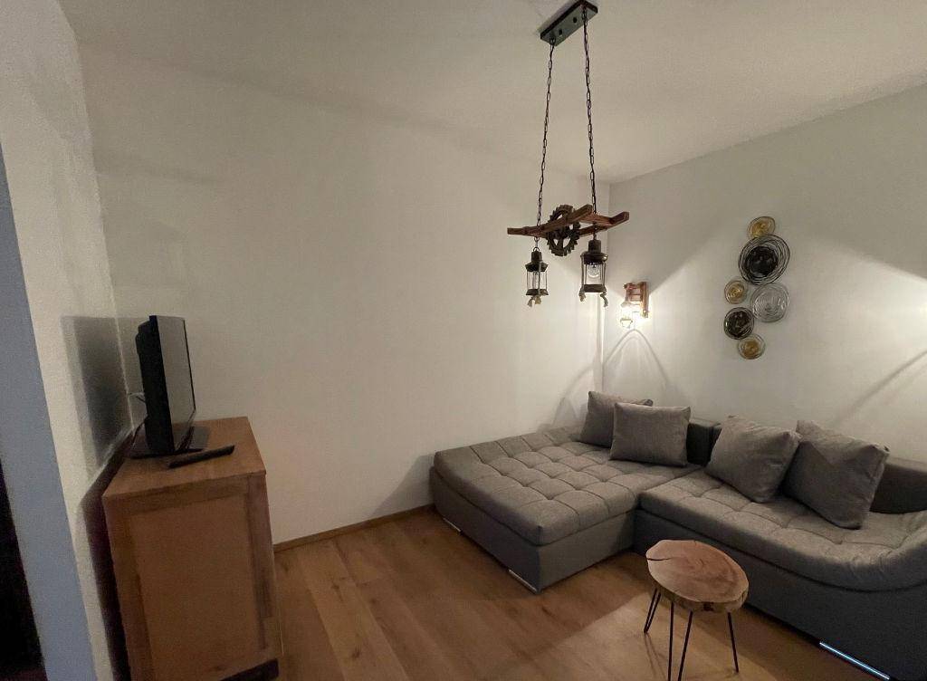 Gemütliches Wohnzimmer mit Ecksofa, Holzboden und rustikaler Deckenlampe, ideal zum Entspannen.