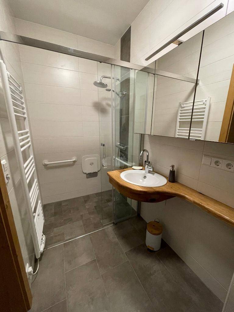 Barrierefreies Badezimmer mit ebenerdiger Dusche, Haltegriffen und modernem Waschtisch.