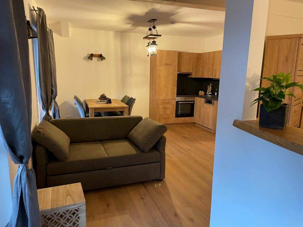 Offener Wohn-Essbereich mit integrierter Holzküche und gemütlichem Sofa, ideal für geselliges Beisammensein.