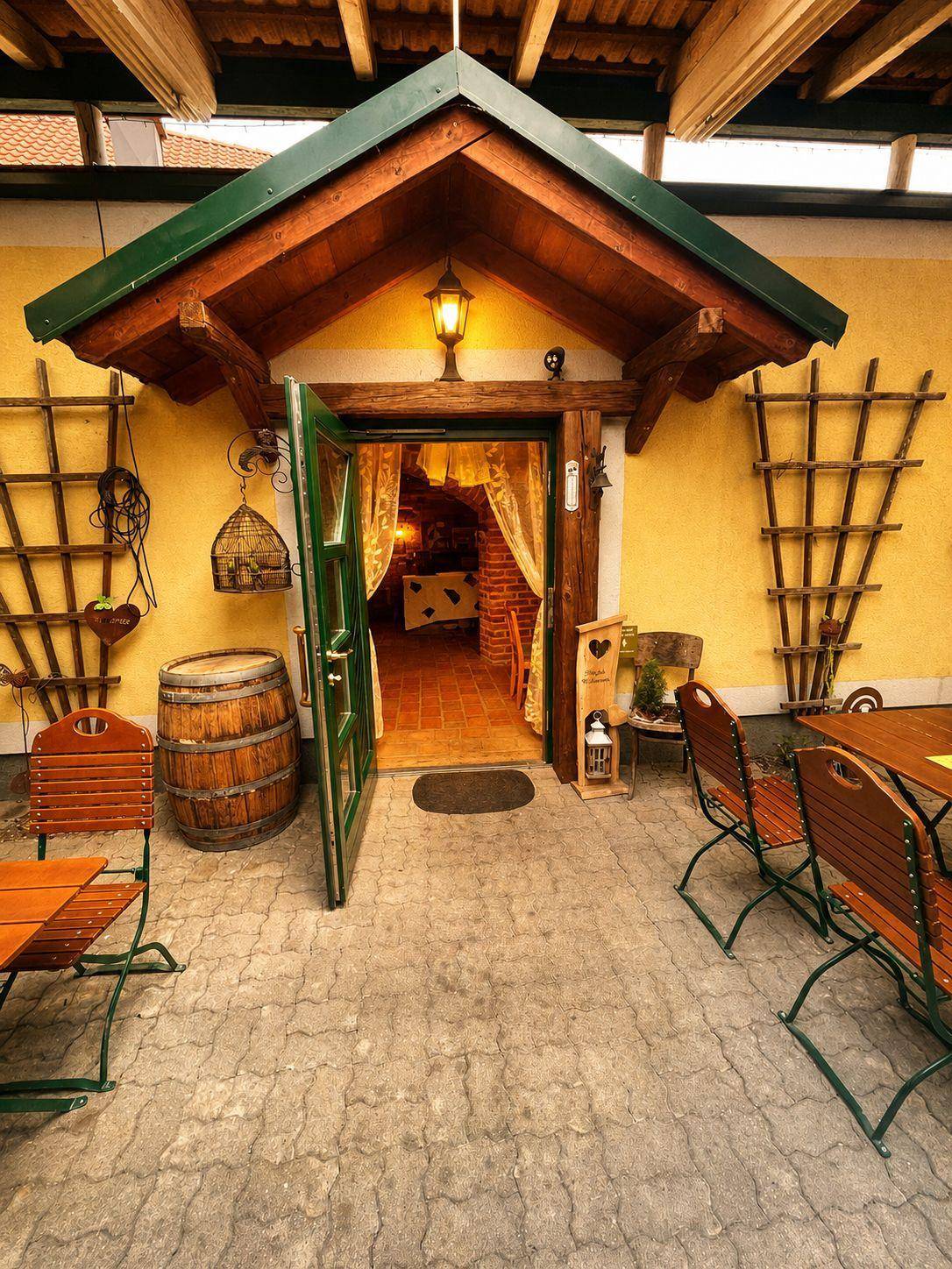 Eingangsbereich mit offener Holztür, umgeben von rustikalen Möbeln und Dekorationen auf einer Terrasse.