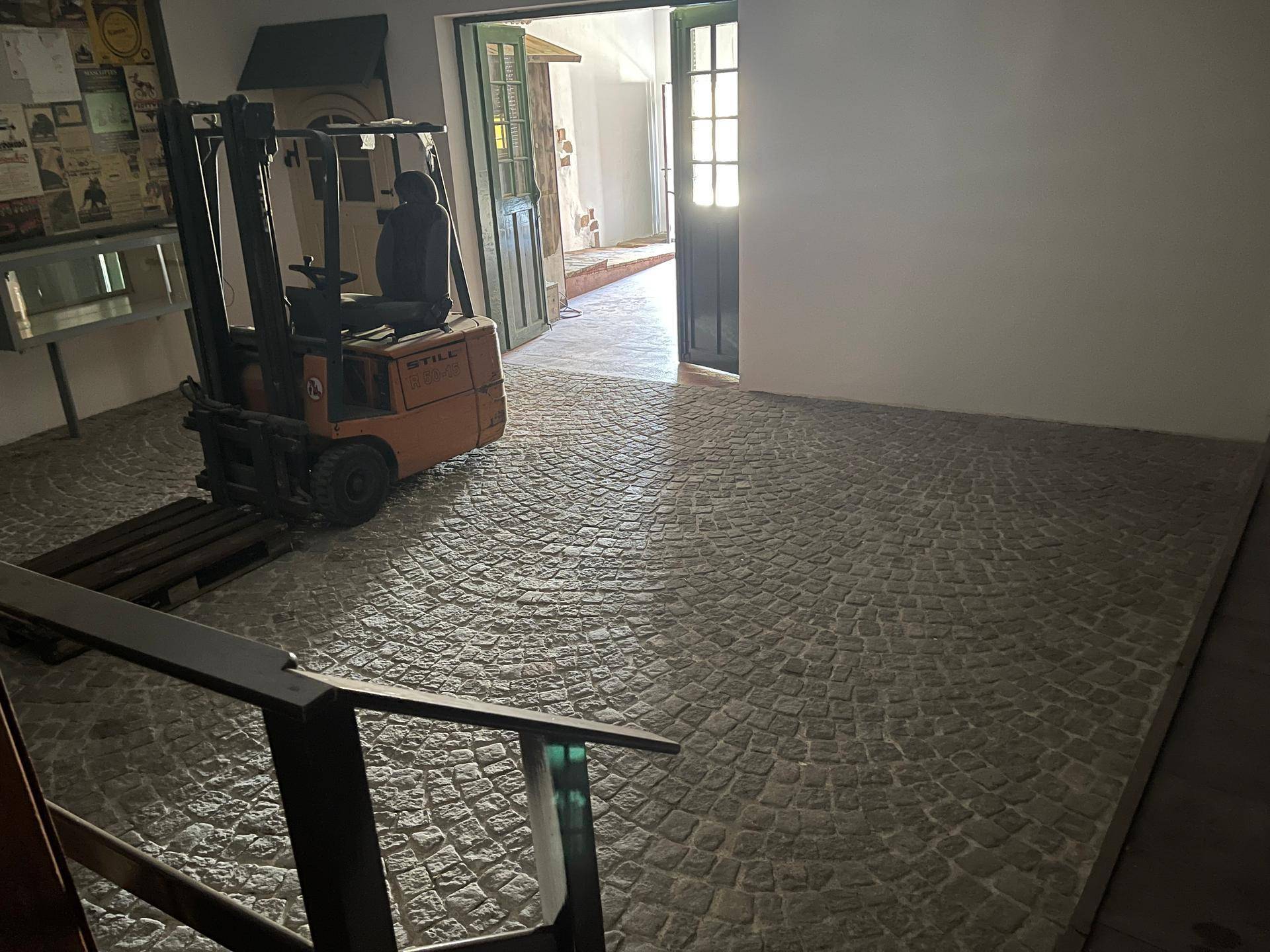 Großer offener Raum mit Kopfsteinpflasterboden und einem Gabelstapler, der auf einen weiteren Bereich blickt.