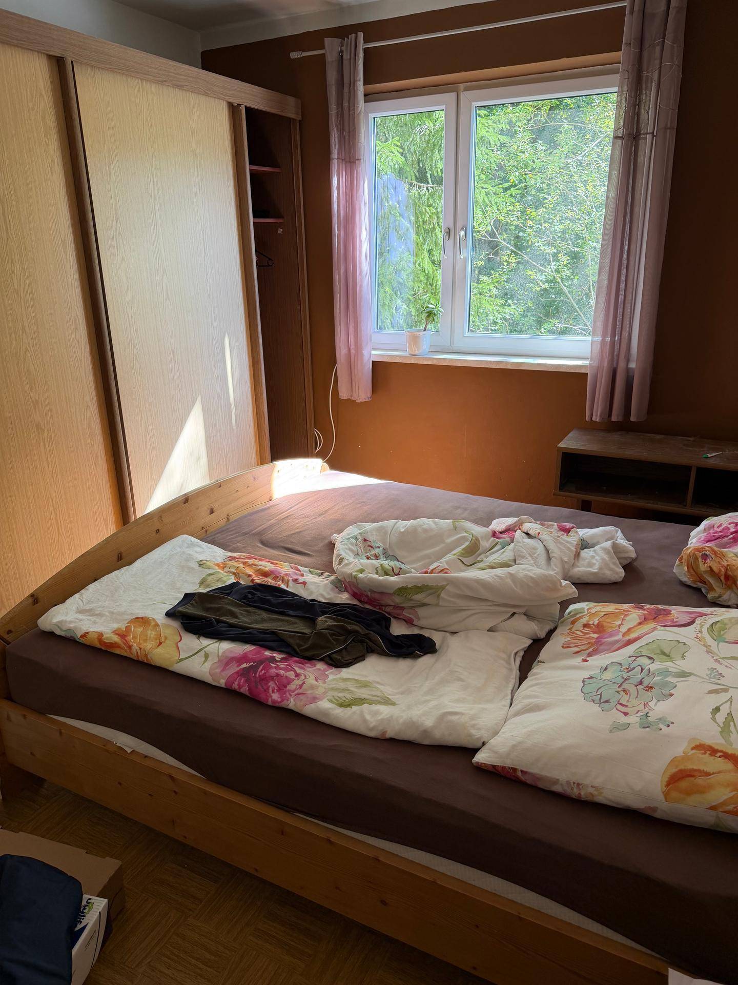 Gemütliches Schlafzimmer mit Holzbett, Schiebetürenschrank und floraler Bettwäsche.