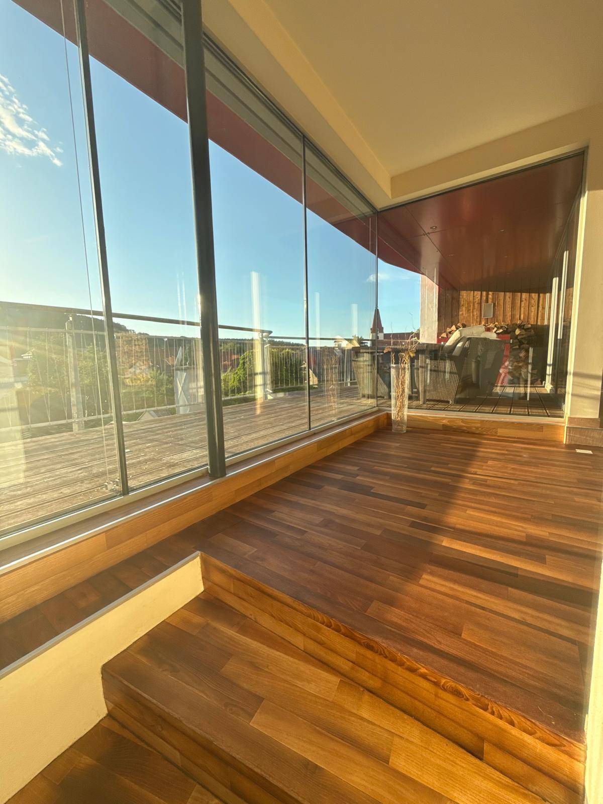 Heller Innenbereich mit Holzboden und großen Glasfronten, die einen weiten Blick auf die Umgebung bieten.
