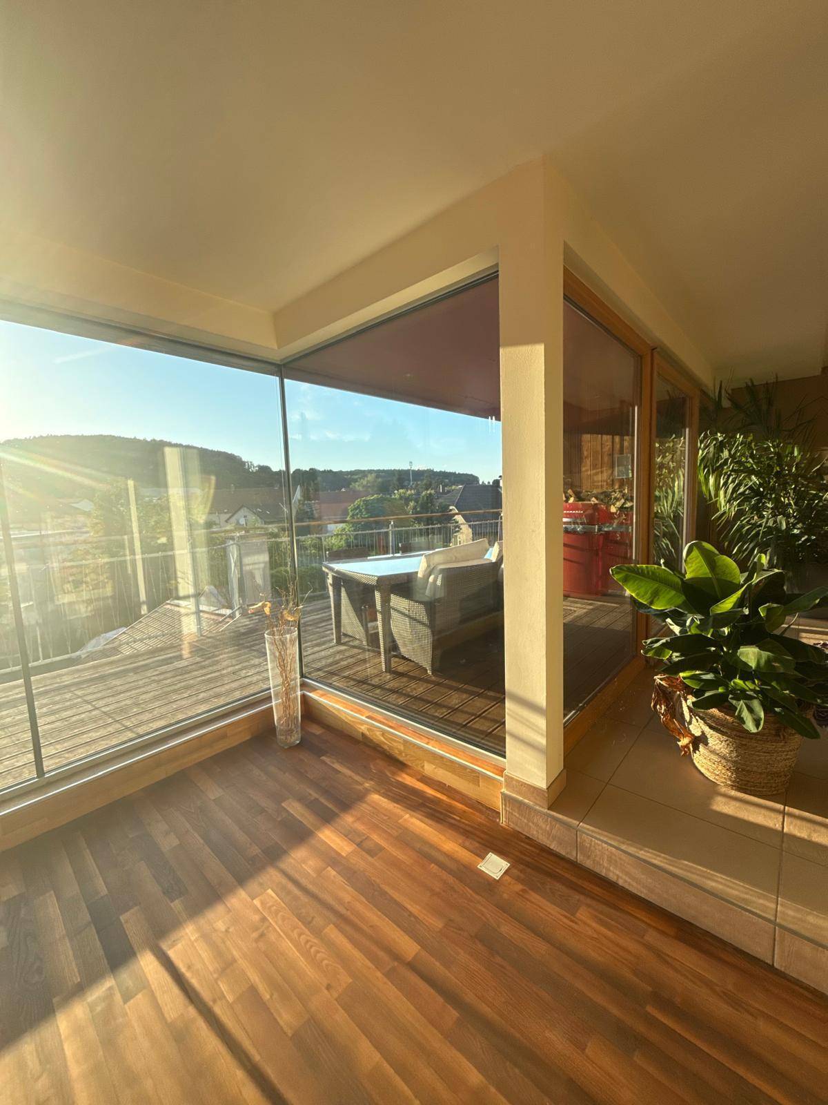 Lichtdurchfluteter Raum mit Pflanzen und Zugang zu einer möblierten Terrasse mit Panoramablick.