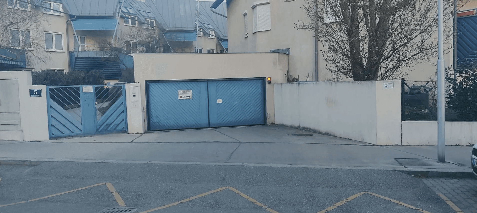 Geschlossene Einfahrt zu einer Tiefgarage mit einem großen blauen Tor und angrenzenden Wohnhäusern.