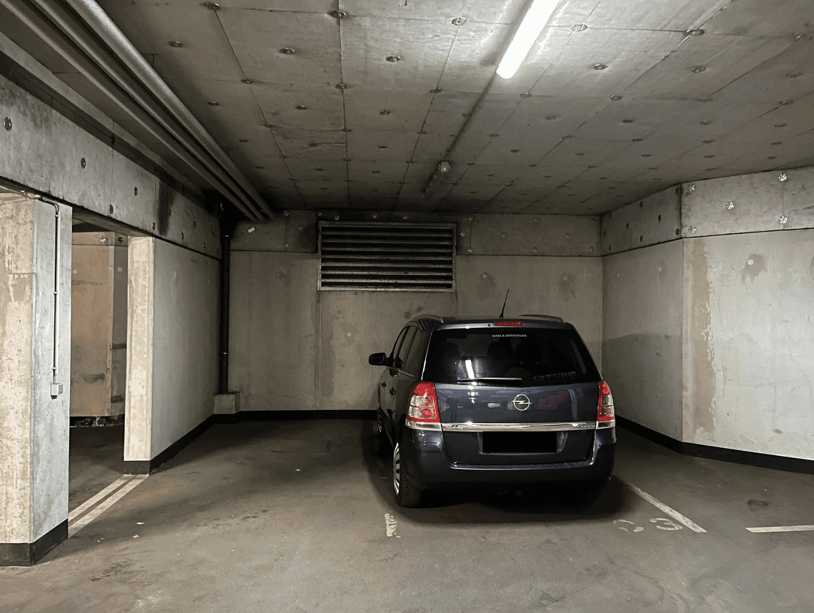 Einzelner Stellplatz in einer Tiefgarage mit rohen Betonoberflächen und Deckenbeleuchtung.
