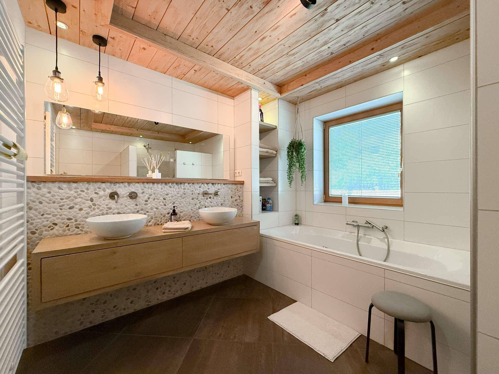 Modernes Badezimmer mit Doppelwaschbecken, Badewanne und Natursteinakzenten.
