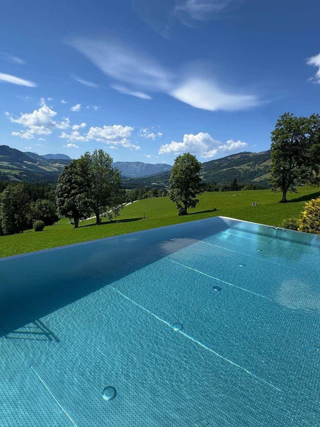 Infinity-Pool mit kristallklarem Wasser und atemberaubendem Panoramablick auf die grüne Bergwelt.