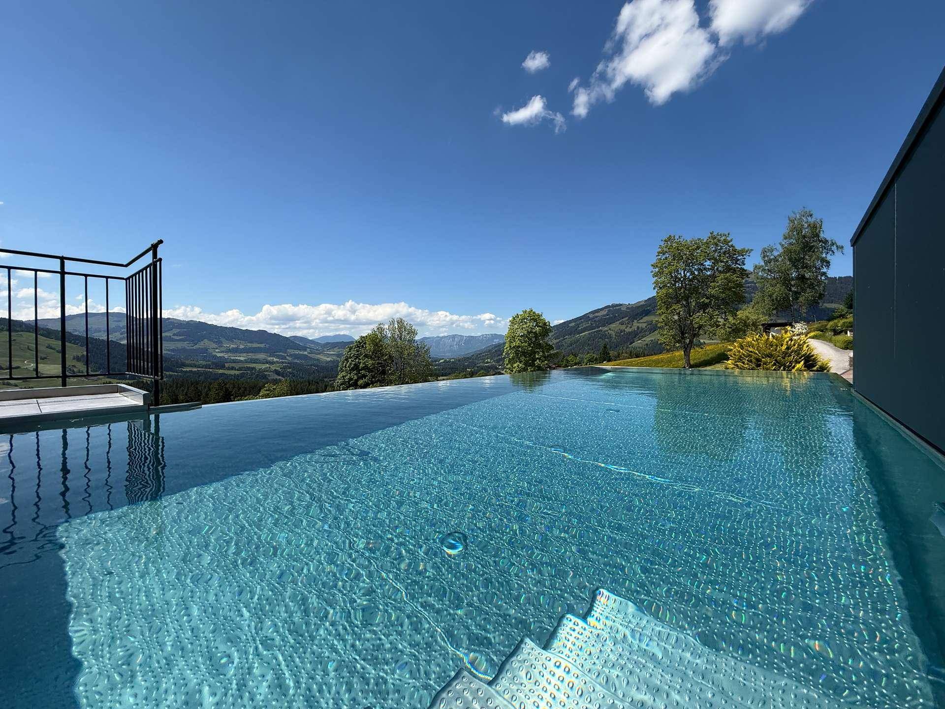 Infinity-Pool mit klarem Wasser und weitem Blick auf die grüne Berglandschaft.