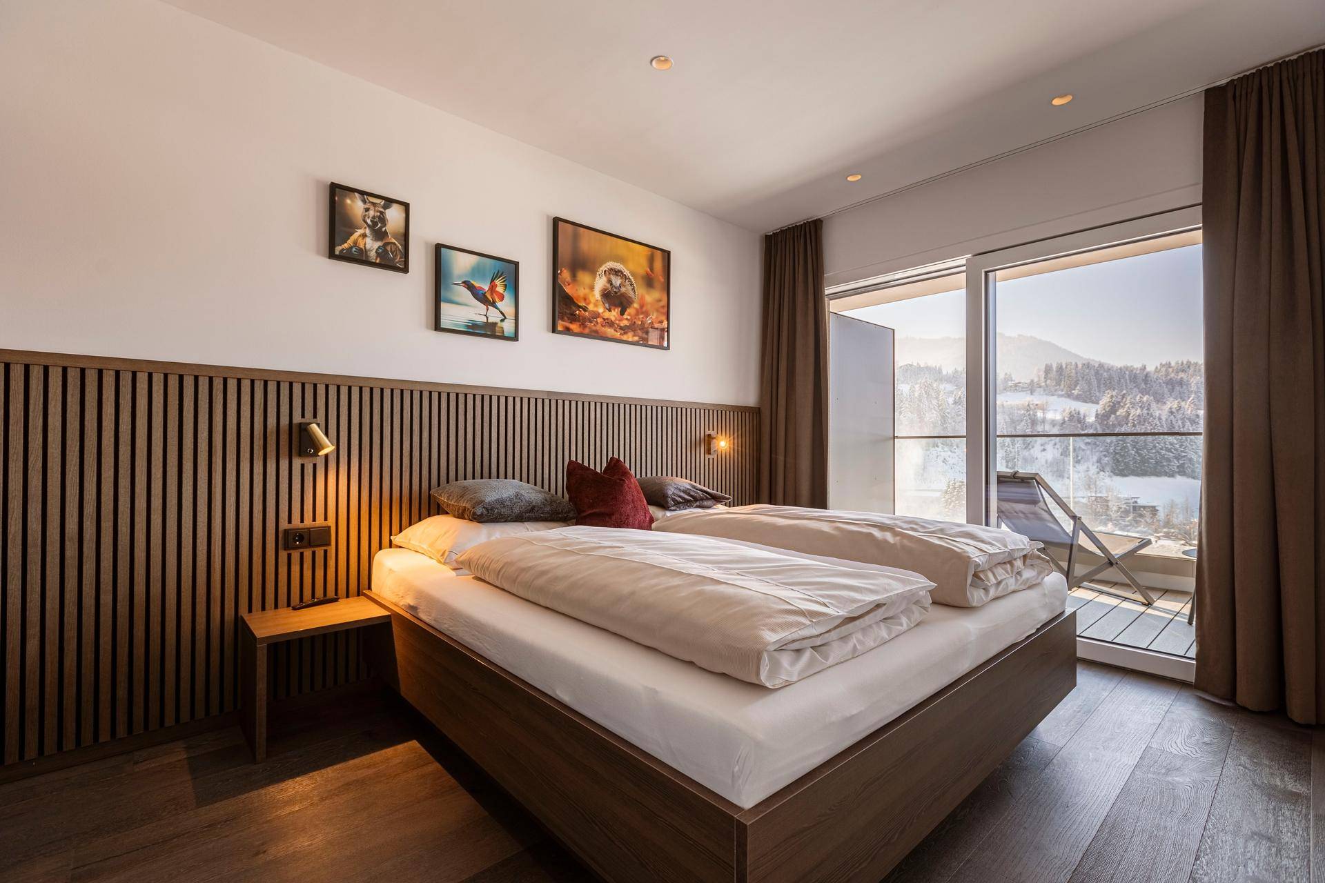 Helles Schlafzimmer mit Doppelbett, Holzvertäfelung und Balkonzugang mit Bergblick.