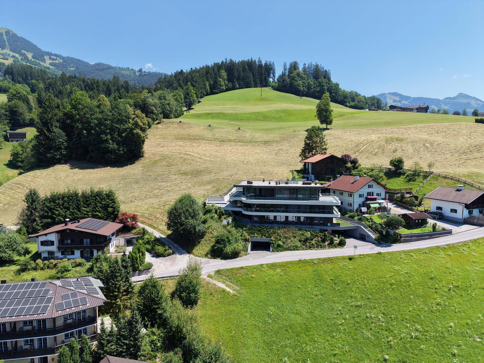 Weitläufige Luftaufnahme der modernen Wohnanlage in idyllischer grüner Hügellandschaft mit umliegenden Häusern.