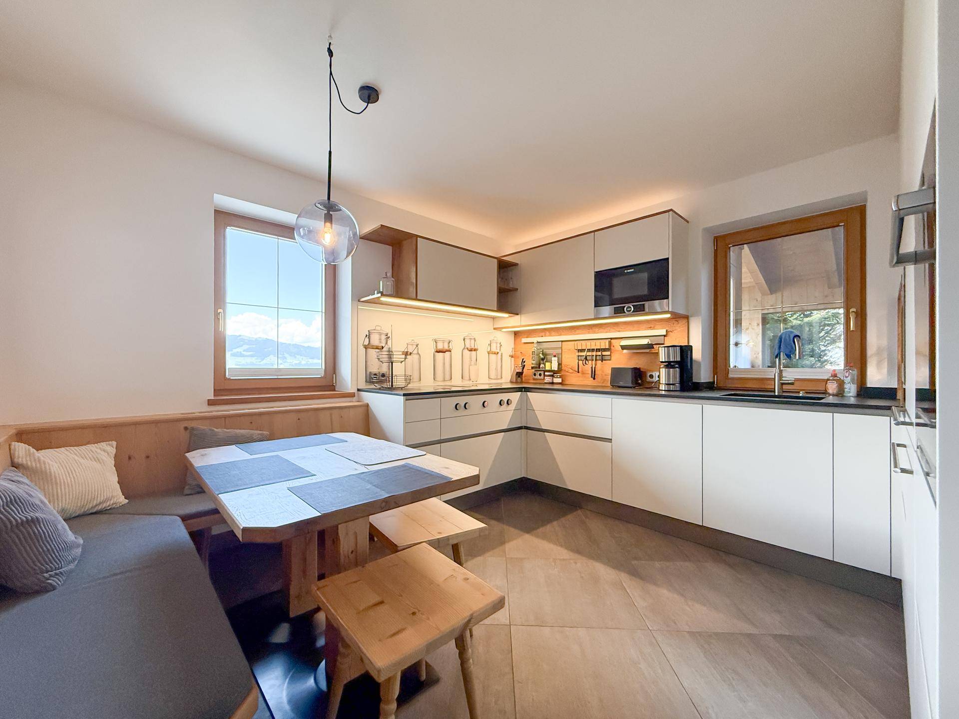 Moderne Küche mit heller Einrichtung, Essbereich und Fenstern mit Bergblick.