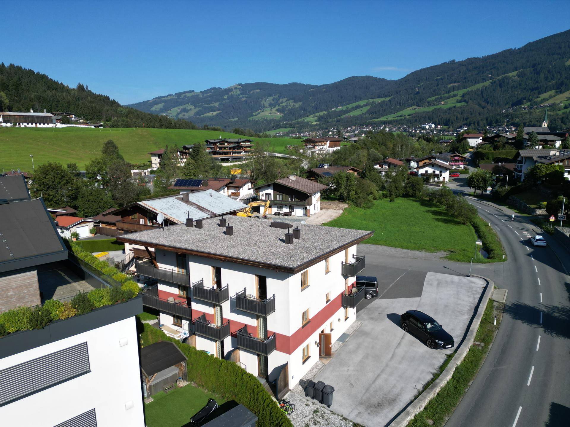 Luftaufnahme des Mehrfamilienhauses mit Parkplätzen und weitem Blick auf die Bergwelt.