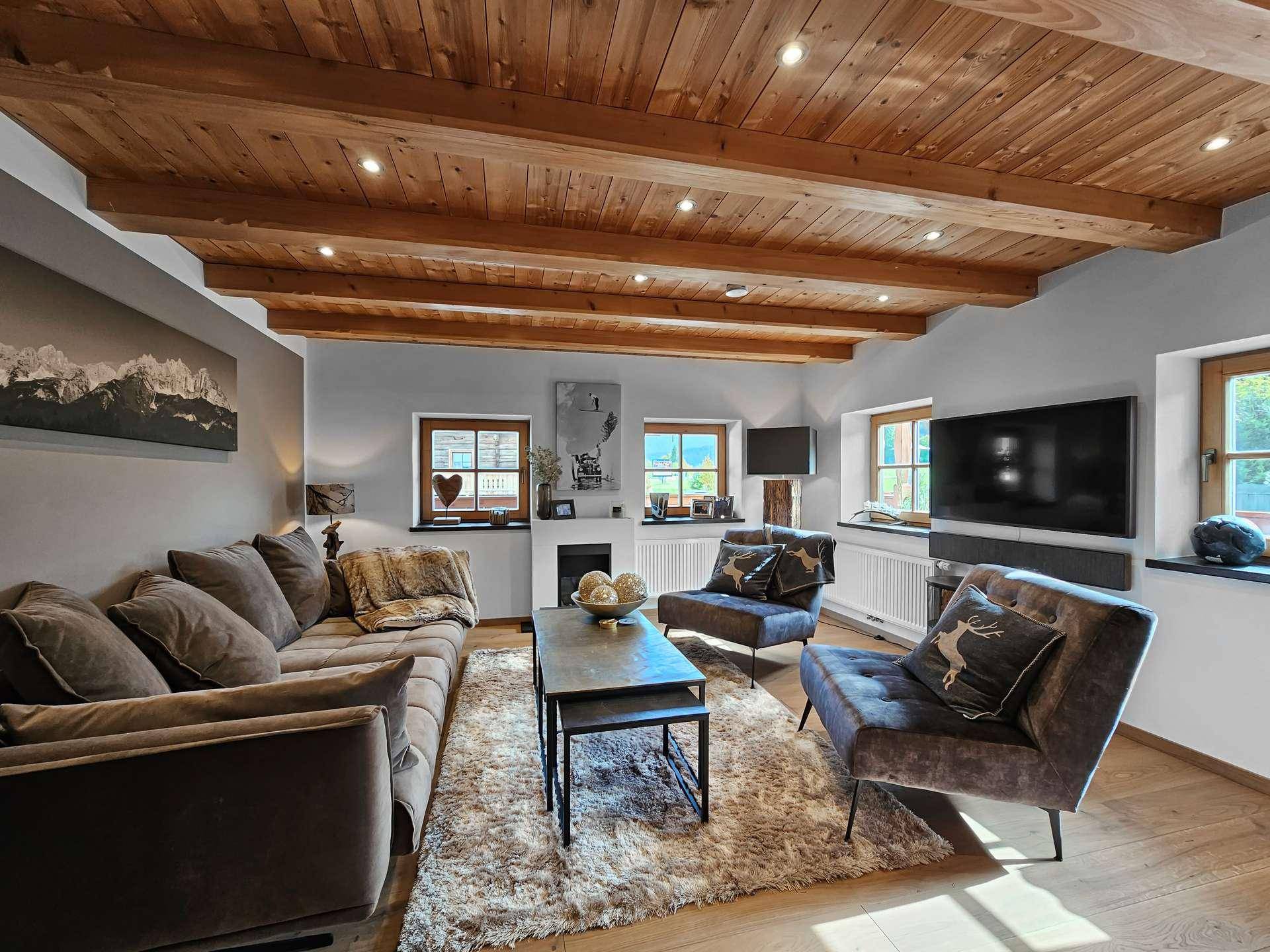 Komfortables Wohnzimmer mit großem Sofa, Teppich und Holzbalkendecke, ideal zum Entspannen.