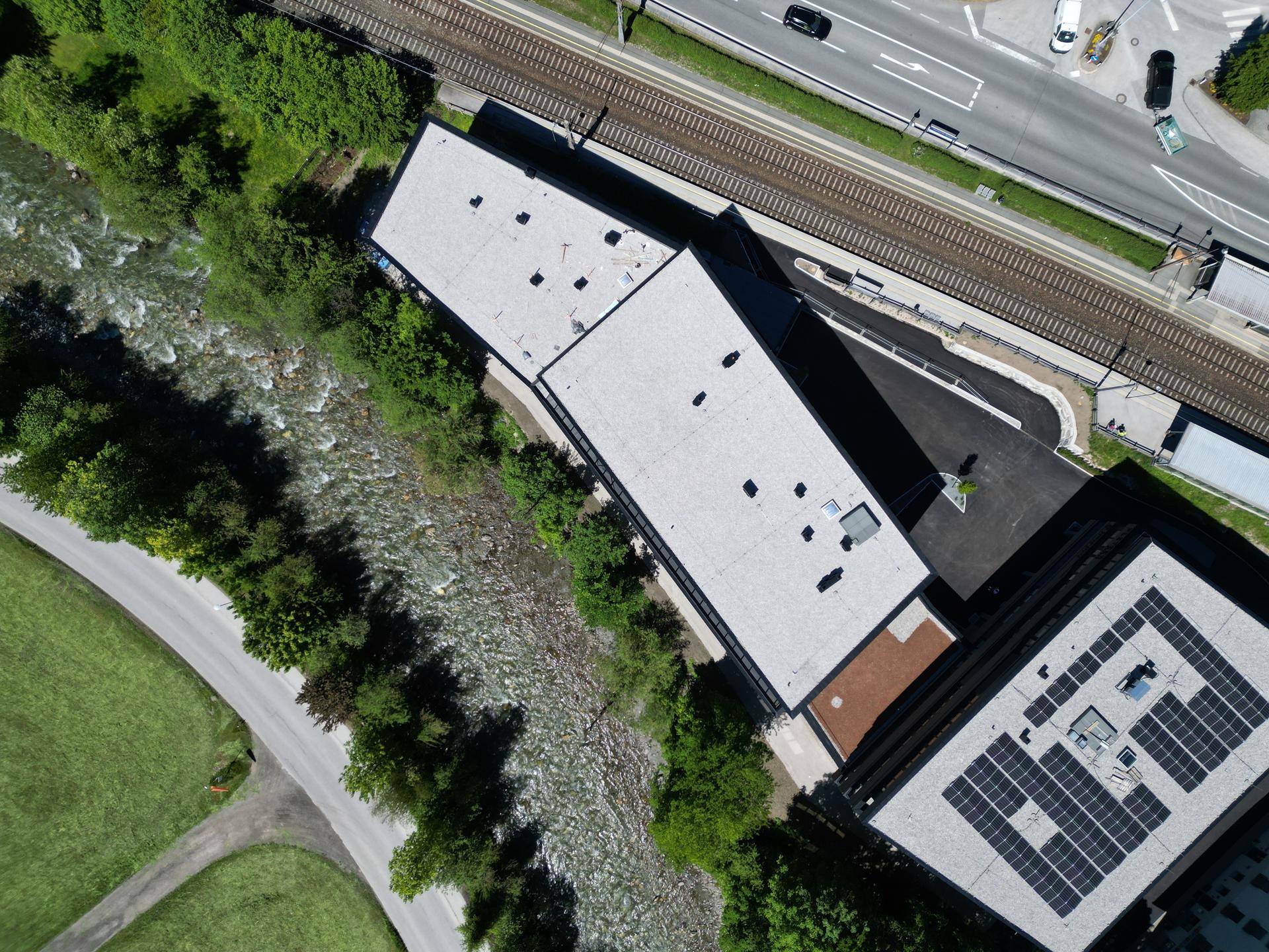 Luftaufnahme eines Gebäudes mit Flachdach und Solaranlage neben einem Fluss und Straße.
