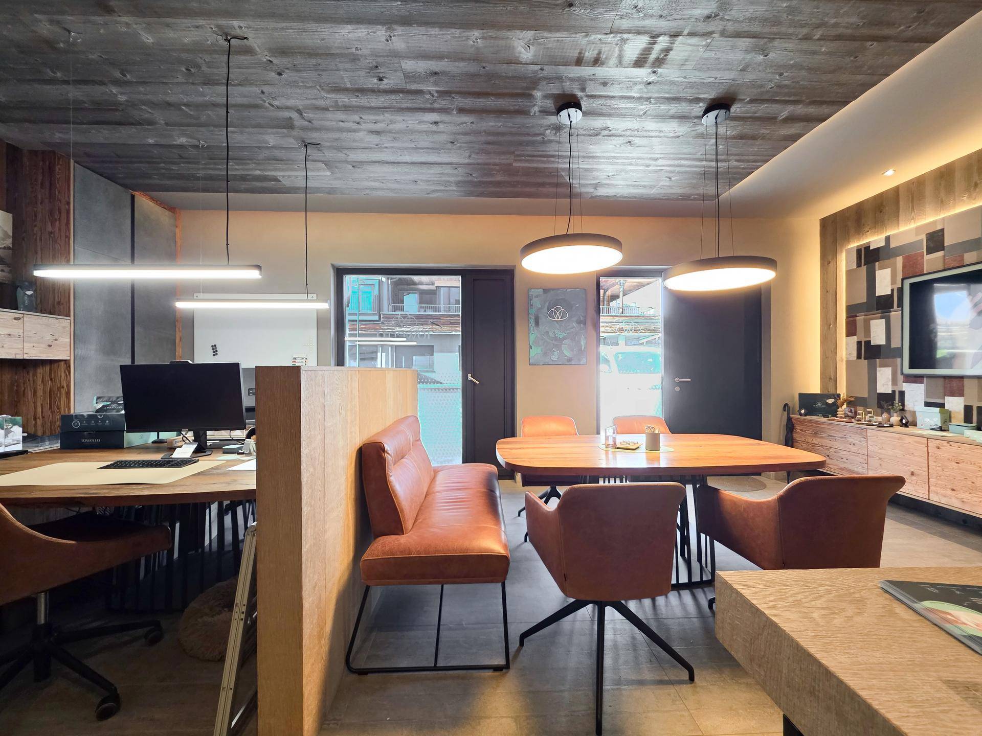 Offener Bürobereich mit Holztisch, bequemen Sitzgelegenheiten und Blick nach draußen, perfekt für Teamarbeit.