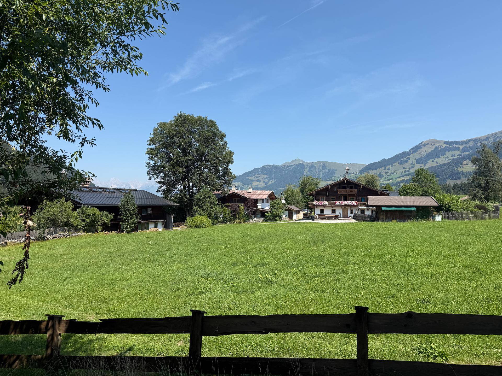 Idyllische Landschaft mit grünen Wiesen, traditionellen Häusern und majestätischen Bergen im Hintergrund.