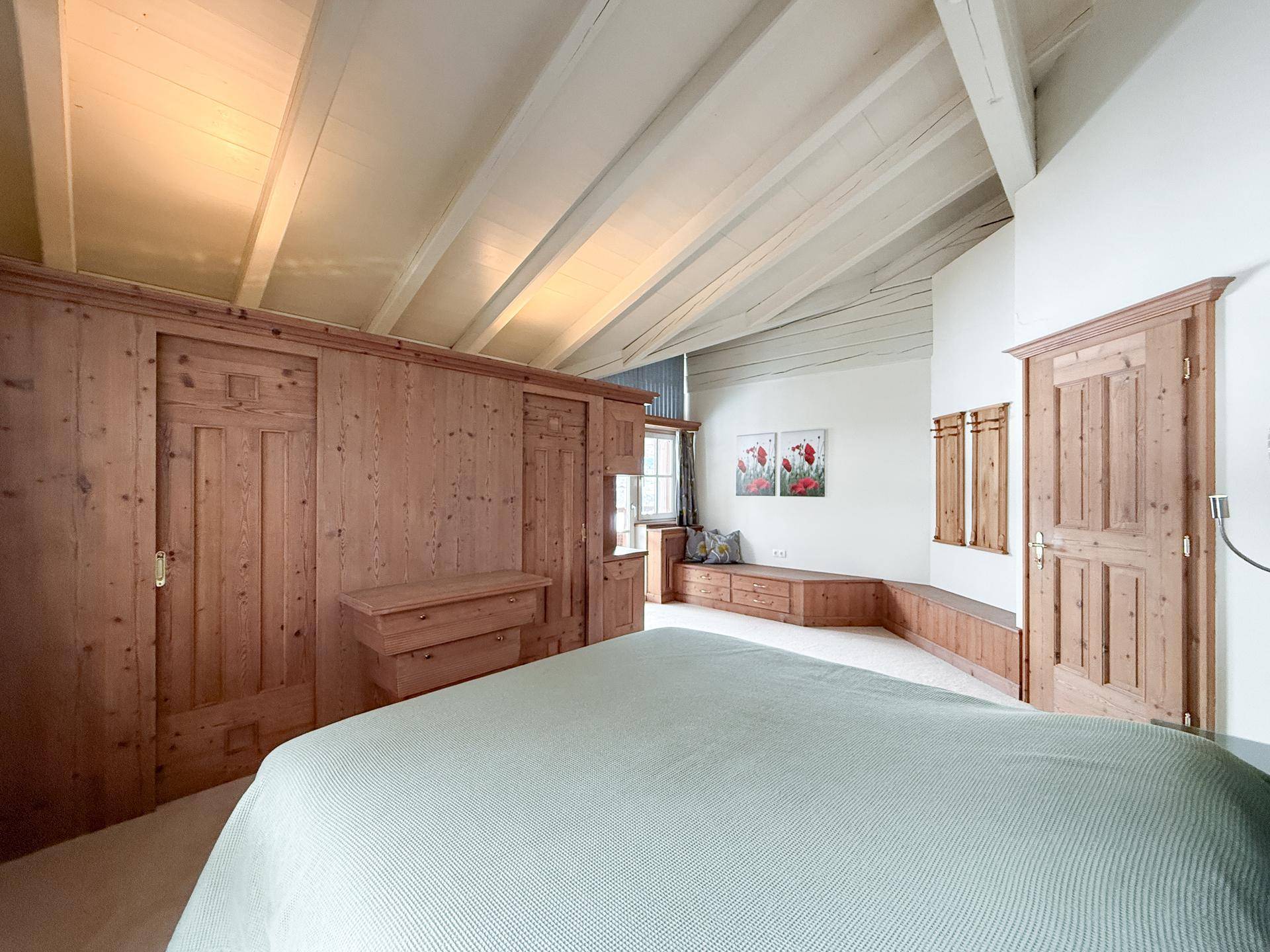 Geräumiges Schlafzimmer mit Dachschräge, Holzeinbauten und hellem Teppichboden.
