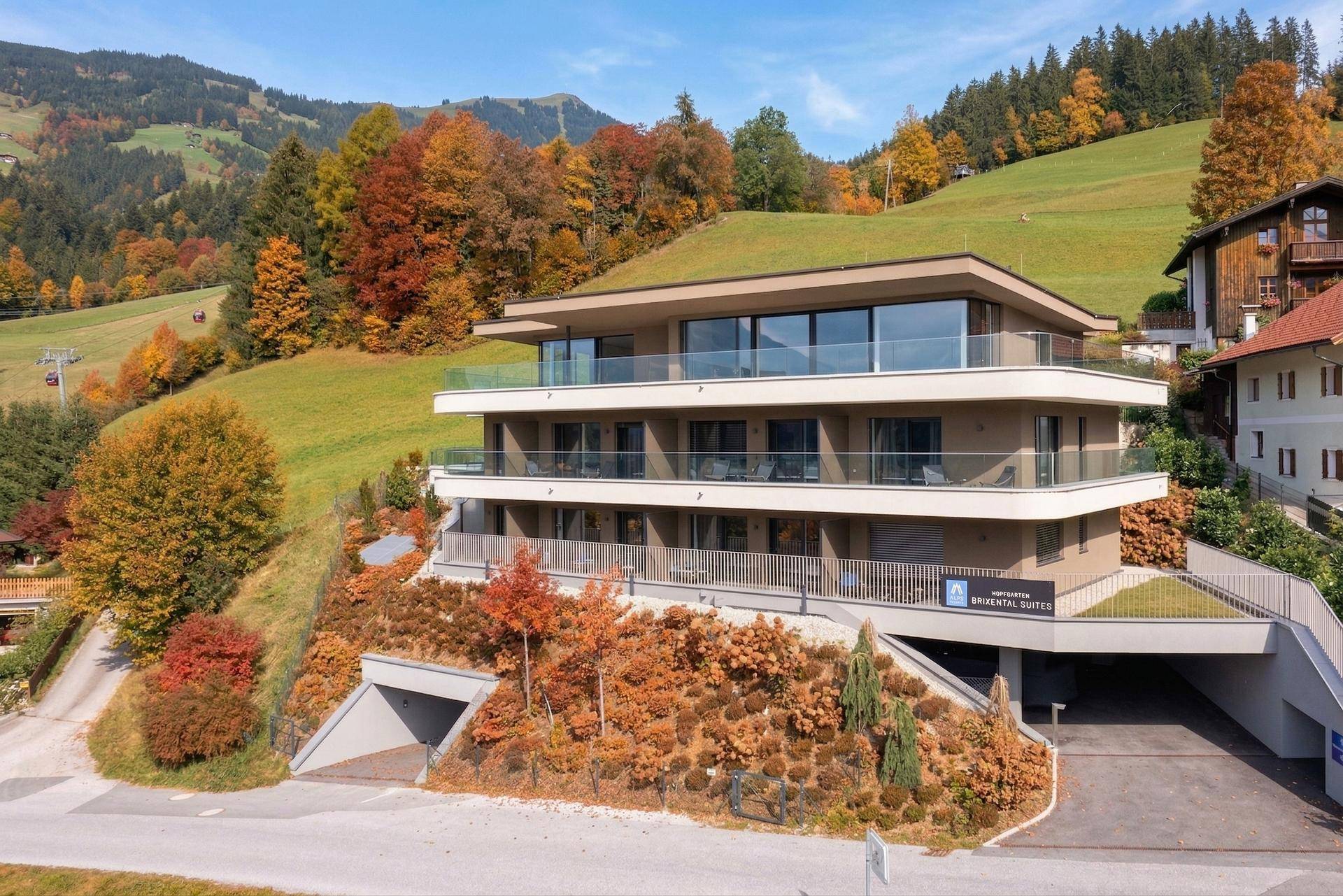 Moderne Wohnanlage im Herbst mit farbenfrohen Bäumen und begrüntem Dach, eingebettet in die Hügellandschaft.